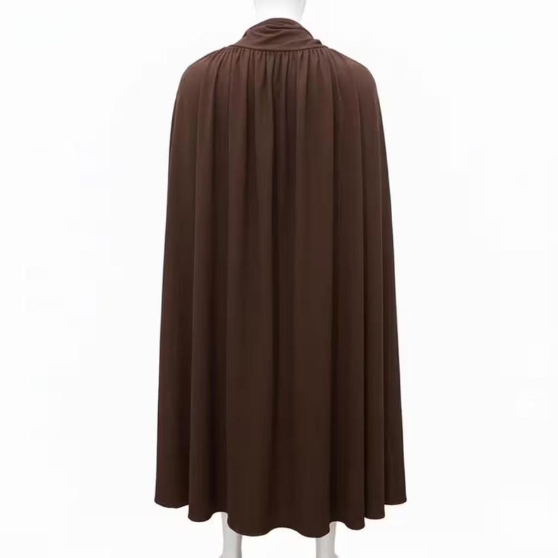 May include: A long, flowing brown cape with a high, gathered neckline. The cape is made of a soft, draping fabric and falls to the ankles. The back view shows vertical folds in the fabric.