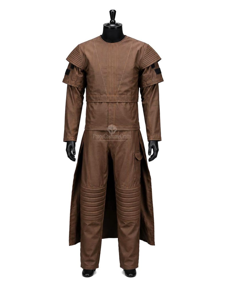 May include: A brown costume comprising a long coat, trousers, and a top with shoulder detailing. The costume features a futuristic design with stitched elements and a belt. The trousers have knee padding and a pocket. The costume is displayed on a black mannequin.
