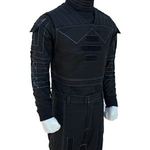 May include: Black jumpsuit with a high collar and long sleeves. The outfit features white stitching details and rectangular patches on the chest, sleeves, and pants. The mannequin is wearing a black outfit with a futuristic design.
