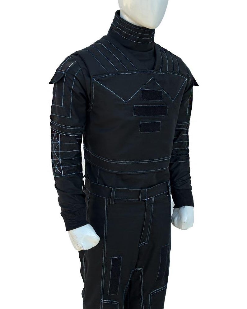 May include: Black jumpsuit with a high collar and long sleeves. The outfit features white stitching details and rectangular patches on the chest, sleeves, and pants. The mannequin is wearing a black outfit with a futuristic design.