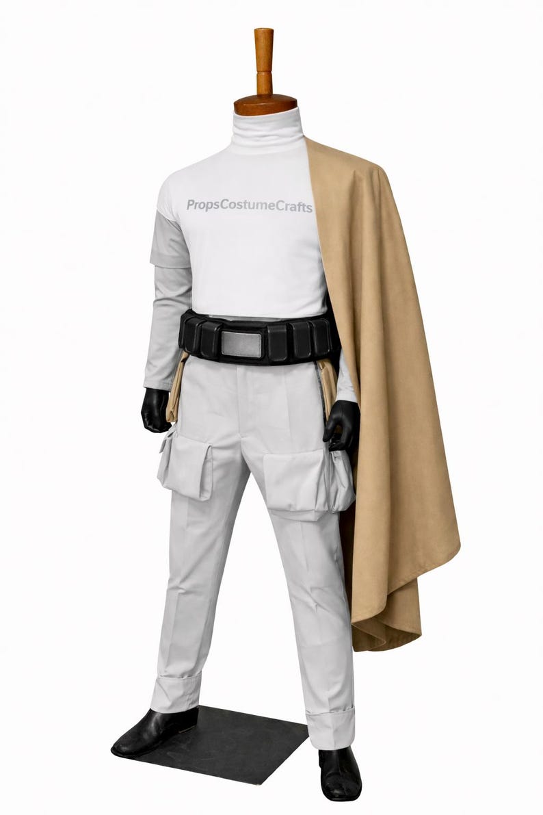 Puede incluir: Un disfraz en un maniqu&iacute;. Presenta una camiseta blanca de cuello alto con el texto "PropsCostumeCrafts", pantalones grises claros con bolsillos, un cintur&oacute;n negro, guantes negros, una capa color canela y zapatos negros. El disfraz se exhibe en un maniqu&iacute;.