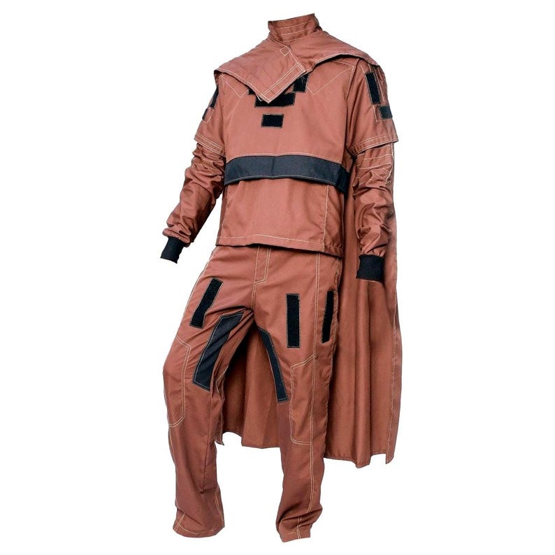 May include: A brown costume with black accents, featuring a jacket with a high collar and a cape, paired with matching pants. The jacket has black patches and a black band across the chest. The pants also have black patches.