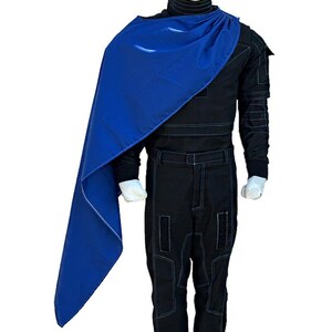May include: A black jumpsuit with white stitching and a high collar is paired with a vibrant blue cape. The cape is draped over the shoulder, creating a striking contrast against the dark attire. The outfit is displayed on a mannequin.