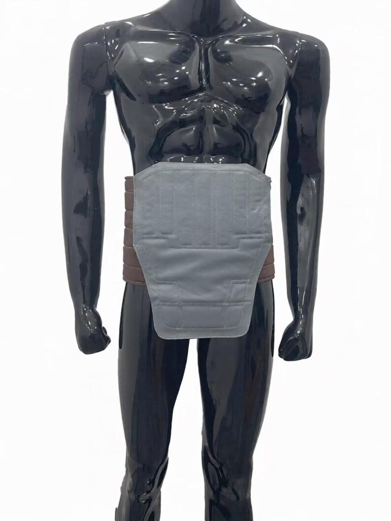 May include: A gray and brown back support belt. The belt has a wide, padded gray section that covers the lower back and abdomen, and a brown band that wraps around the waist. The mannequin is black.