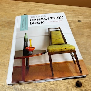 Puede incluir: El pequeño libro de tapicería de Shelly Miller Leer, una guía para principiantes en tapicería artesanal. La portada presenta una silla con rayas amarillas y negras con un marco de madera.