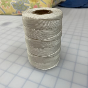 May include: A spool of white nylon cord, wound tightly and ready for use.