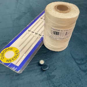 May include: A spool of white nylon tufting twine with a label that reads "OSBORNE No. 4700-T1/2 NYLON TUFTING TWINE CS OSBORNE & CO. HARRISON, NJ 07029".  The spool is next to a package of needles and two blue buttons.