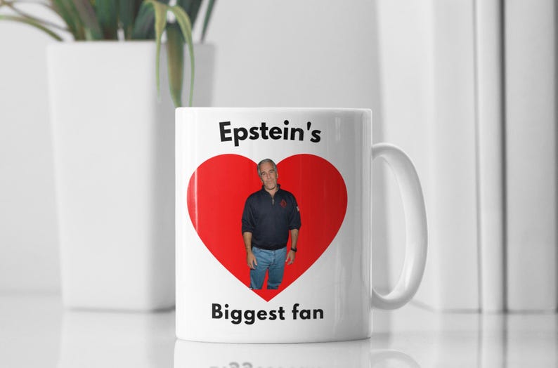 May include: White ceramic mug featuring a red heart graphic and the text "Epstein's Biggest fan." The heart contains a photo of a man in a navy blue shirt and jeans. The mug has a white handle.
