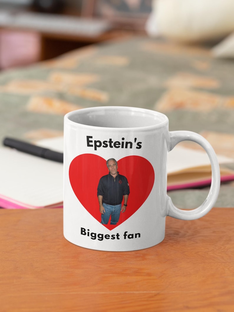 May include: White ceramic mug with a black handle. The mug features a red heart with a photo of a man inside. The text "Epstein's Biggest fan" is printed on the mug.
