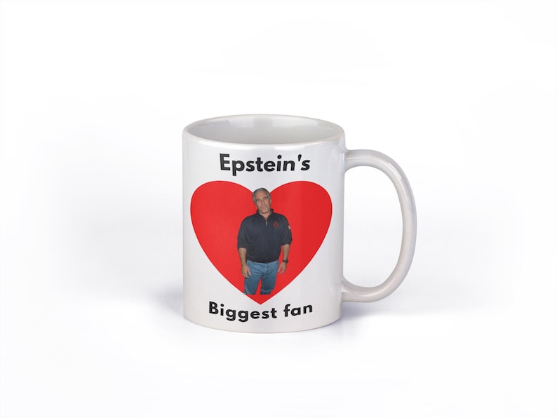 May include: White ceramic mug with a handle. The mug features the text "Epstein's Biggest fan" with a red heart graphic containing a photo of a man.