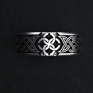May include: A silver-colored ring with a Celtic knot design. The ring features intricate interwoven patterns and a central knot motif. The band is wide and has a polished finish, suitable for a variety of occasions.