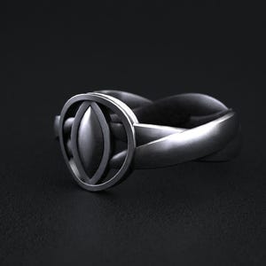 May include: A silver ring with a unique design. The ring features a central oval shape within a circular frame, set on a twisted band. The ring is made of a shiny, metallic material, and is set against a dark background.