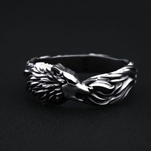 May include: A silver-toned ring featuring a detailed wolf head design. The wolf's head is sculpted with intricate fur and facial features. The ring's band has a textured, flowing design, creating a bold and striking piece of jewelry.
