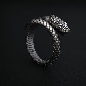 May include: A silver-colored ring in the shape of a snake. The snake's head is detailed with scales and a slightly open mouth. The ring is marked with "925" on the inside. The ring is a unique piece of jewelry.