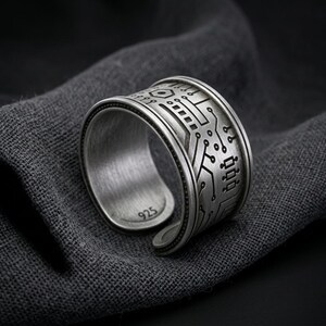 Könnte beinhalten: Ein breiter, offener Silberring mit einem dunklen, geätzten Leiterplattenmuster auf der Außenseite. Die Innenseite des Rings ist aus gebürstetem Silber und deutlich mit der Zahl 925 geprägt, was auf Sterlingsilber hinweist.