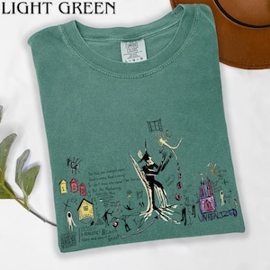 Puede incluir: Una camiseta de cuello redondo color verde claro con un estampado gr&aacute;fico que incluye ilustraciones en negro, amarillo, rojo y morado de figuras abstractas, una casa y un castillo. El texto dice "The floor plan changed again" y "UNREALIZED."