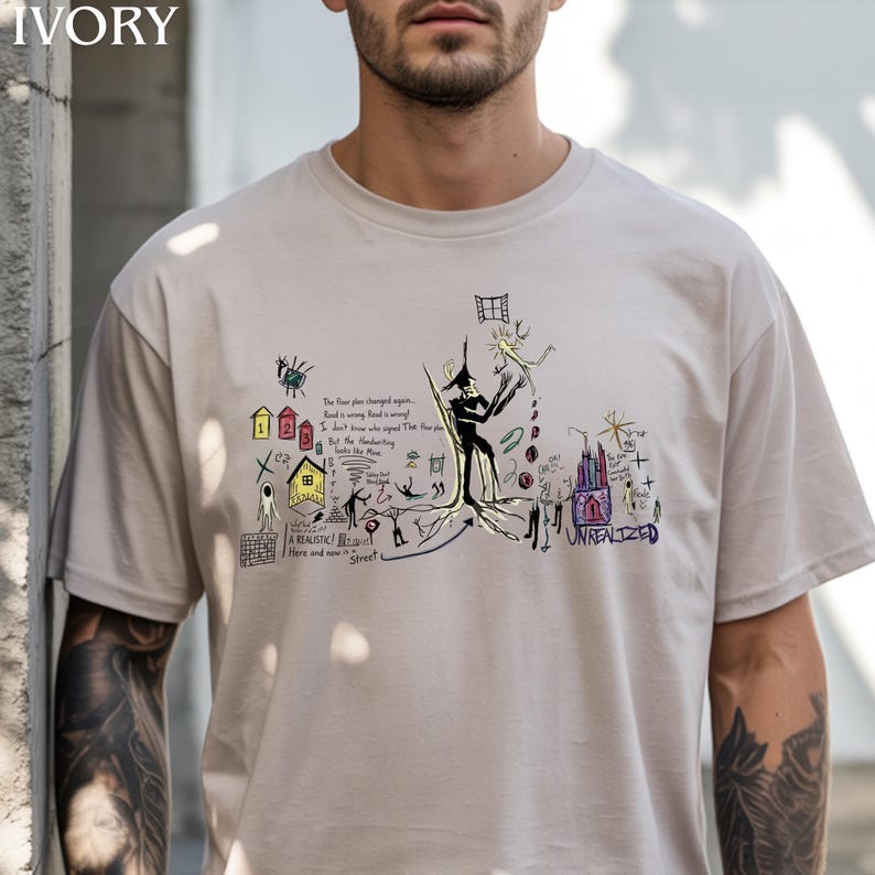 Puede incluir: Una camiseta de color marfil de manga corta con un complejo estampado gr&aacute;fico multicolor. El dise&ntilde;o incluye varios bocetos dibujados a mano, figuras abstractas, peque&ntilde;as casas numeradas 1, 2, 3 y texto escrito a mano, incluyendo UNREALIZED.