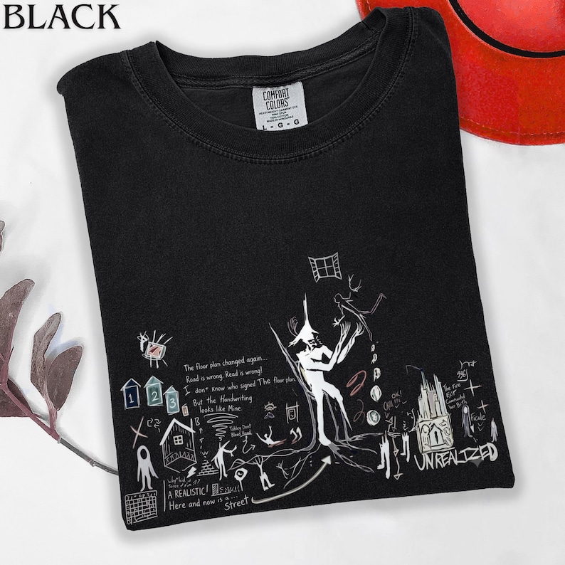 Puede incluir: Una camiseta negra de manga corta con un estampado gr&aacute;fico blanco que incluye varias ilustraciones dibujadas a mano, como una figura central, iconos de casas peque&ntilde;as y el texto The floor plan changed again y UNREALIZED.