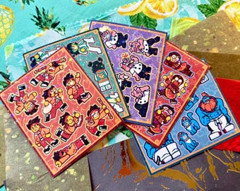 May include: A collection of colorful sticker sheets featuring cartoon characters in various poses. The stickers have a red, purple, blue, and green border. The background includes patterned fabric with fruit designs.