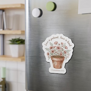 Puede incluir: Un imán floral con una ilustración en acuarela de una maceta de terracota llena de flores rosas y follaje verde. El imán tiene el texto "Love is patient, love is kind" y "1 Corinthians 13:4".