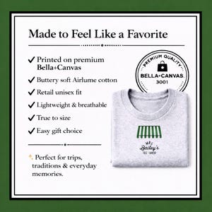 May include: A light grey t-shirt featuring the text "Mrs. Bailey's Tee Shop" and a green awning design. The shirt is made of soft Airlume cotton and is lightweight and breathable. The image also includes text about the shirt's features.