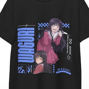 May include: Black t-shirt featuring a graphic of an anime character in a red and white outfit. The word "WAGURI" is printed vertically in blue, with additional text and design elements. The shirt is hanging on a wooden hanger.