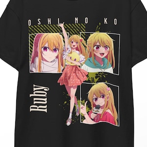 以下が含まれることがあります： アニメ「推しの子」のルビーが描かれた黒いTシャツ。デザインにはルビーの複数の画像が含まれており、上部に「OSHI NO KO」、左側に縦書きで「Ruby」と書かれています。木製のハンガーに掛けられています。