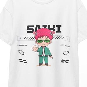 Puede incluir: Camiseta blanca con un personaje de dibujos animados con pelo rosa y gafas verdes. La palabra "SAIKI" está impresa en letras negras. Debajo, una barra horizontal con las palabras "CUTENESS" y "ACTIVATED".