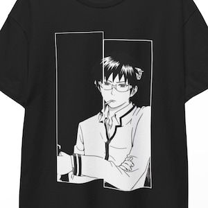 Puede incluir: Camiseta negra con una ilustración en blanco y negro de estilo anime de una persona con gafas y uniforme escolar. El gráfico está enmarcado dentro de un rectángulo blanco. La camiseta está colgada en una percha de madera.