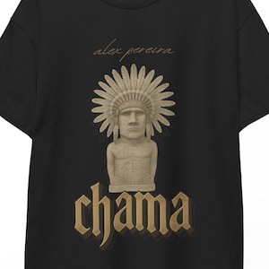 Può includere: T-shirt nera con una grafica di una statua con un copricapo di piume e la parola "chama" in un font stilizzato. Il nome "alex pereira" è sopra la statua. La maglietta è appesa a una gruccia di legno.