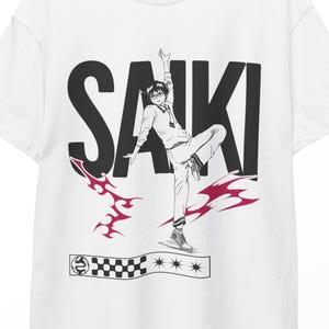Puede incluir: Camiseta blanca con un gráfico en blanco y negro de una persona en una pose dinámica, con la palabra "SAIKI" en letras negras en negrita. Diseños rojos en forma de llama y un patrón de tablero de ajedrez con estrellas completan el diseño.