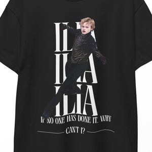 May include: Black t-shirt with a graphic of a figure skater and the word "ILIA" in white. The text "IF NO ONE HAS DONE IT. WHY CAN'T I?" is below the skater. The shirt is hanging on a wooden hanger.