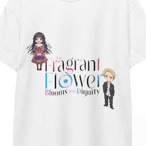 Peut inclure: T-shirt blanc avec l'inscription "The Fragrant Flower Blooms with Dignity" dans un design coloré, accompagné d'illustrations de dessins animés d'une fille et d'un garçon. Le t-shirt est suspendu à un cintre en bois.