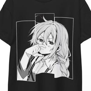 Op de afbeelding: Zwart T-shirt met een zwart-wit anime-stijl illustratie van een persoon met lang haar en een bril, in een bedachtzame pose. De afbeelding is omlijst door een witte rand. Het T-shirt hangt aan een houten hanger.