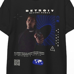 Könnte beinhalten: Schwarzes T-Shirt mit dem Text "DETROIT BECOME HUMAN" über einem Bild einer Person, die eine Waffe hält. Das Shirt zeigt auch den Text "JUST A MACHINE" und ein Zitat über Freiheit. Eine blau-weiße Grafik befindet sich auf der rechten Seite.