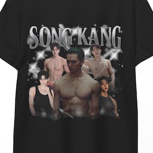 Könnte beinhalten: Schwarzes T-Shirt mit einer Grafik von Song Kang und dem Namen "SONG KANG" in silbernem Text. Die Grafik enthält mehrere Bilder von Song Kang. Das T-Shirt hängt an einem Holzbügel.