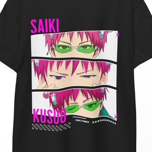 Puede incluir: Camiseta negra con un gráfico de un personaje de anime con pelo rosa y gafas verdes. El texto "SAIKI KUSUO" está impreso en rosa. El diseño incluye tres paneles con diferentes expresiones faciales.