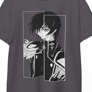 May include: A charcoal gray t-shirt featuring a black and white anime-style illustration of a character within a rectangular frame. The character has dark hair and is wearing a detailed uniform. The shirt is hanging on a wooden hanger.