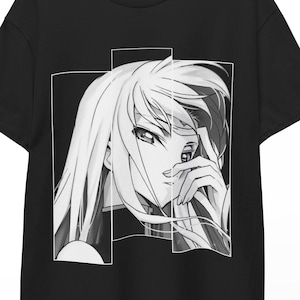 Può includere: T-shirt nero con un'illustrazione in bianco e nero in stile anime di una donna con i capelli lunghi. La grafica è incorniciata da linee bianche. La maglietta è appesa a una gruccia di legno.