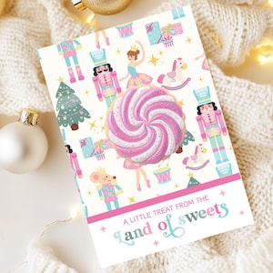 May include: A greeting card with a whimsical design featuring a large pink and white swirled lollipop. The card is decorated with illustrations of nutcrackers, ballerinas, and a Christmas tree. Text reads "A little treat from the land of sweets."