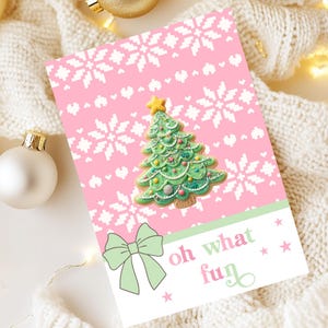 May include: A Christmas card with a pink background featuring white snowflakes and a green Christmas tree design. The card includes a green bow and the words "oh what fun" in a playful font. Decorative ornaments and lights are in the background.
