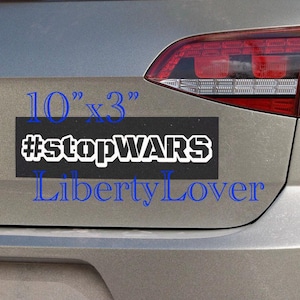 May include: A black rectangular bumper sticker, 10" x 3", with the white text "#stopWARS" and the blue text "Liberty Lover". The sticker is affixed to the rear of a silver vehicle.