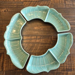Puede incluir: Un conjunto de cuatro fuentes de cerámica turquesa dispuestas en forma circular. Cada fuente tiene una forma curva única con un diseño segmentado y un acabado brillante. Las fuentes están colocadas sobre una superficie de madera.