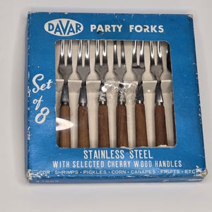 Puede incluir: Un juego de ocho tenedores de fiesta de acero inoxidable con mangos de madera de cerezo, empaquetados en una caja de cartón azul. La caja presenta el texto DAVAR PARTY FORKS, Set of 8, y STAINLESS STEEL WITH SELECTED CHERRY WOOD HANDLES FOR SHRIMPS, PICKLES, CORN, CANAPES, FRUITS, ETC.