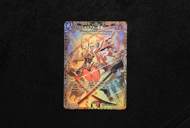 K&ouml;nnte beinhalten: Sammelkarte mit einer gold-orangenen Illustration einer Kriegerin mit einem Schwert. Die Karte hat japanischen Text und die Zahl "6000" unten. Der Hintergrund ist schwarz.