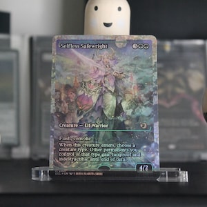 May include: A holographic trading card titled "Selfless Safewright" featuring an Elf Warrior illustration. The card is displayed in a clear acrylic stand. The card's artwork has a fantasy theme with shades of purple, green, and blue. The card's text is visible.