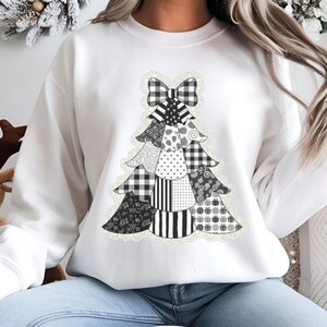 May include: White sweatshirt featuring a black and white patchwork Christmas tree design. The tree is composed of various patterns including polka dots, stripes, and gingham. A black and white bow sits at the top of the tree.