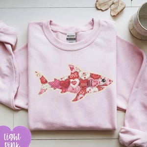Op de afbeelding: Lichtroze sweatshirt met een haaienontwerp gemaakt van harten en het woord "LOVE". De tekst "light pink" staat in een hartvormige afbeelding linksonder. De sweatshirt is een casual stijl.