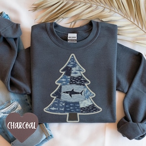 May include: Charcoal grey sweatshirt with a Christmas tree design. The tree is made up of blue patches with fish and shark illustrations. The word "CHARCOAL" is on a heart-shaped tag. The sweatshirt is a crew neck style.