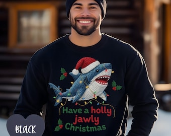 Puede incluir: Una sudadera negra de manga larga con el gráfico de un tiburón azul que lleva un gorro de Papá Noel rojo y blanco, envuelto en luces navideñas. El texto dice Have a holly jawly Christmas, junto a iconos de acebo y bayas rojas.